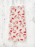 A waffle-weave kitchen tea towel with a pattern of red horses with a light beige background, folded lengthwise in half, on a textured white surface.