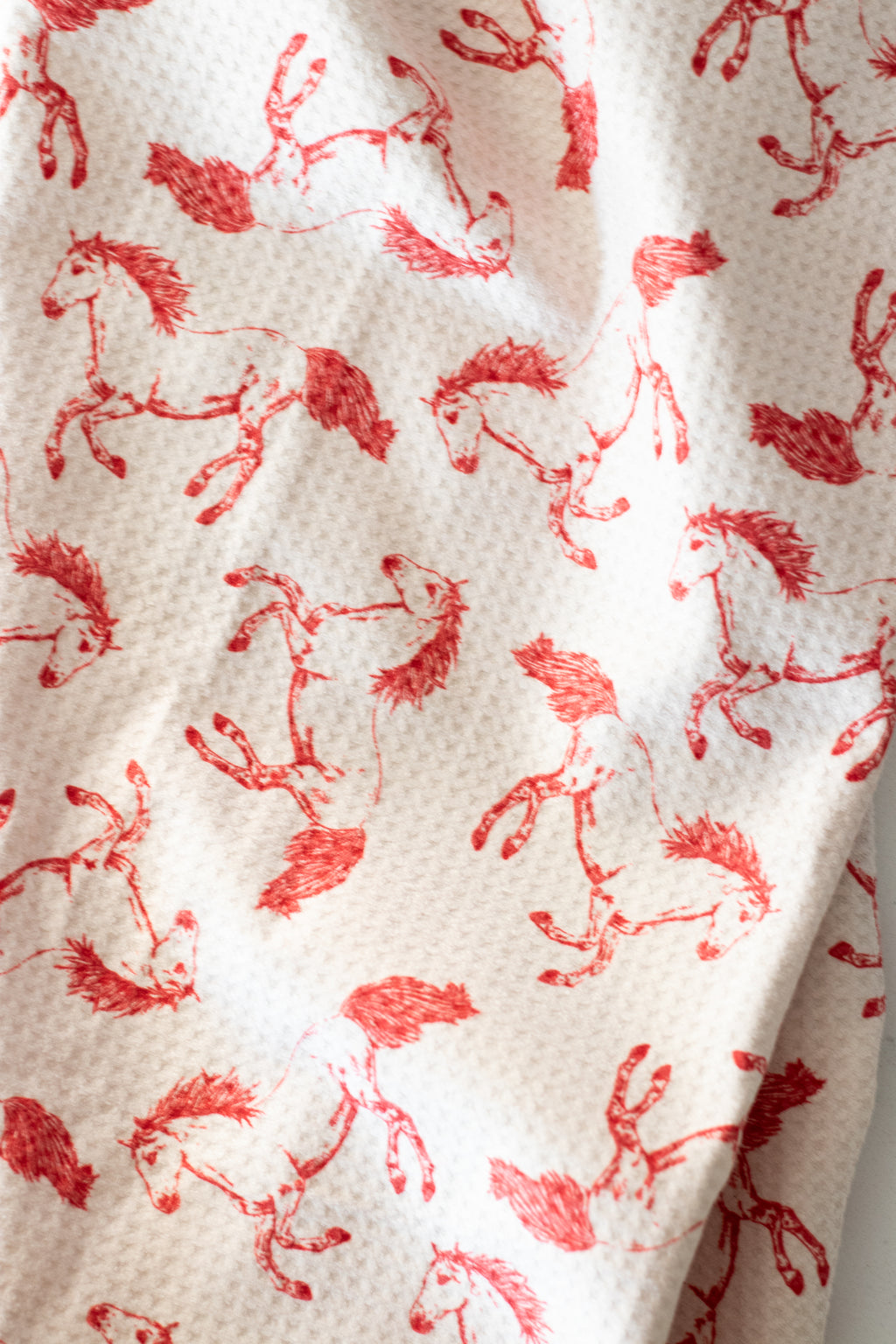 Close-up of a waffle weave tea towel with a red horse pattern on a light beige background