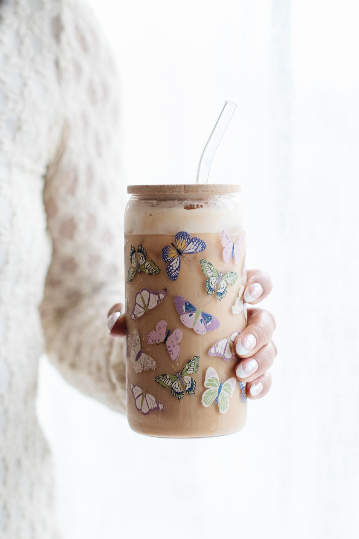 Person holding a can glass with a butterfly design against a white background