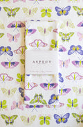 A folded white kitchen Tea Towel with a colorful butterfly print in lime green, indigo and purple, wrapped in a white paper belly band labeled 'ASPECT HOME GOODS',laid flat on a matching butterfly-patterned background.