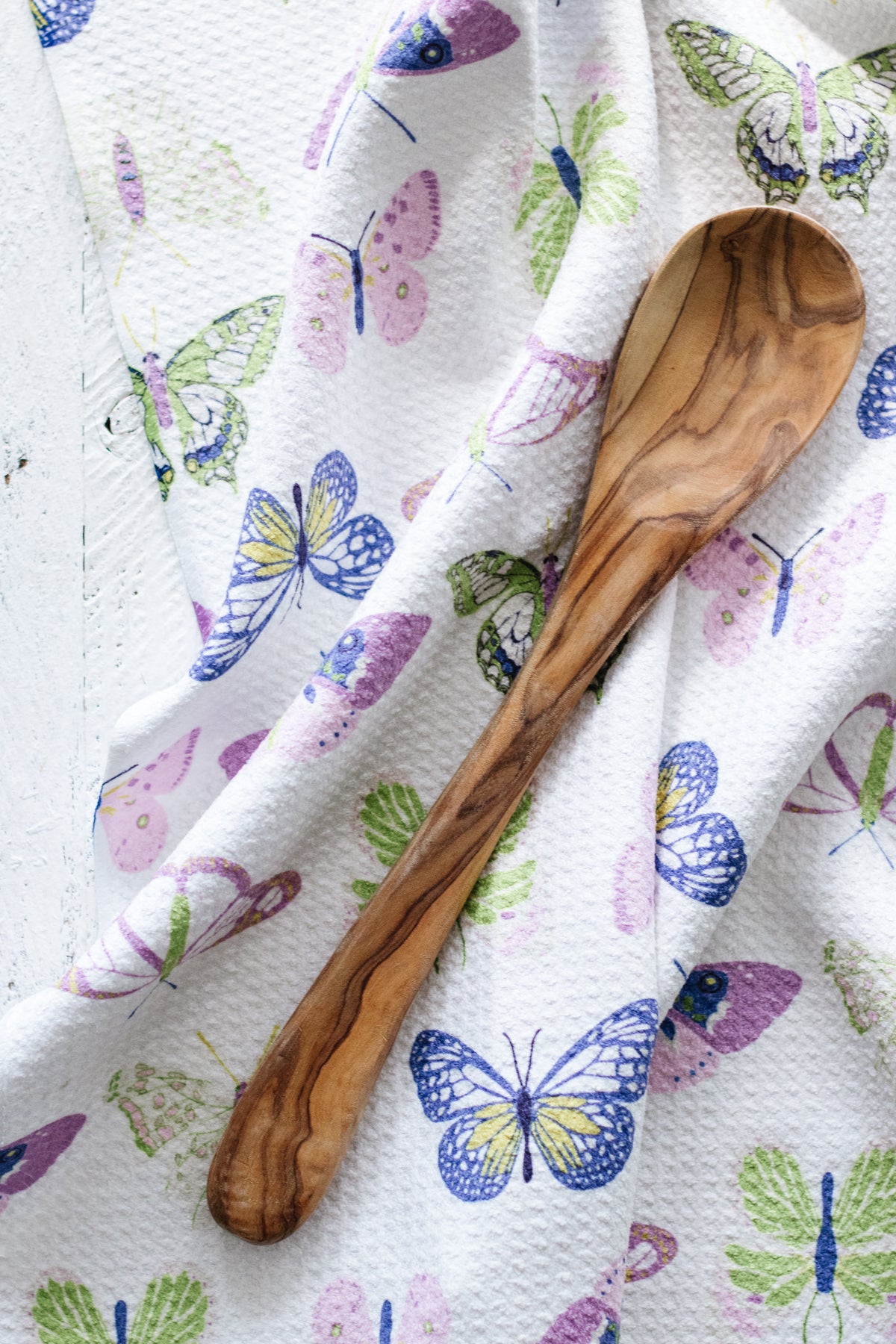 Wooden spoon on a colorful butterfly-patterned waffle-weave kitchen tea towel.