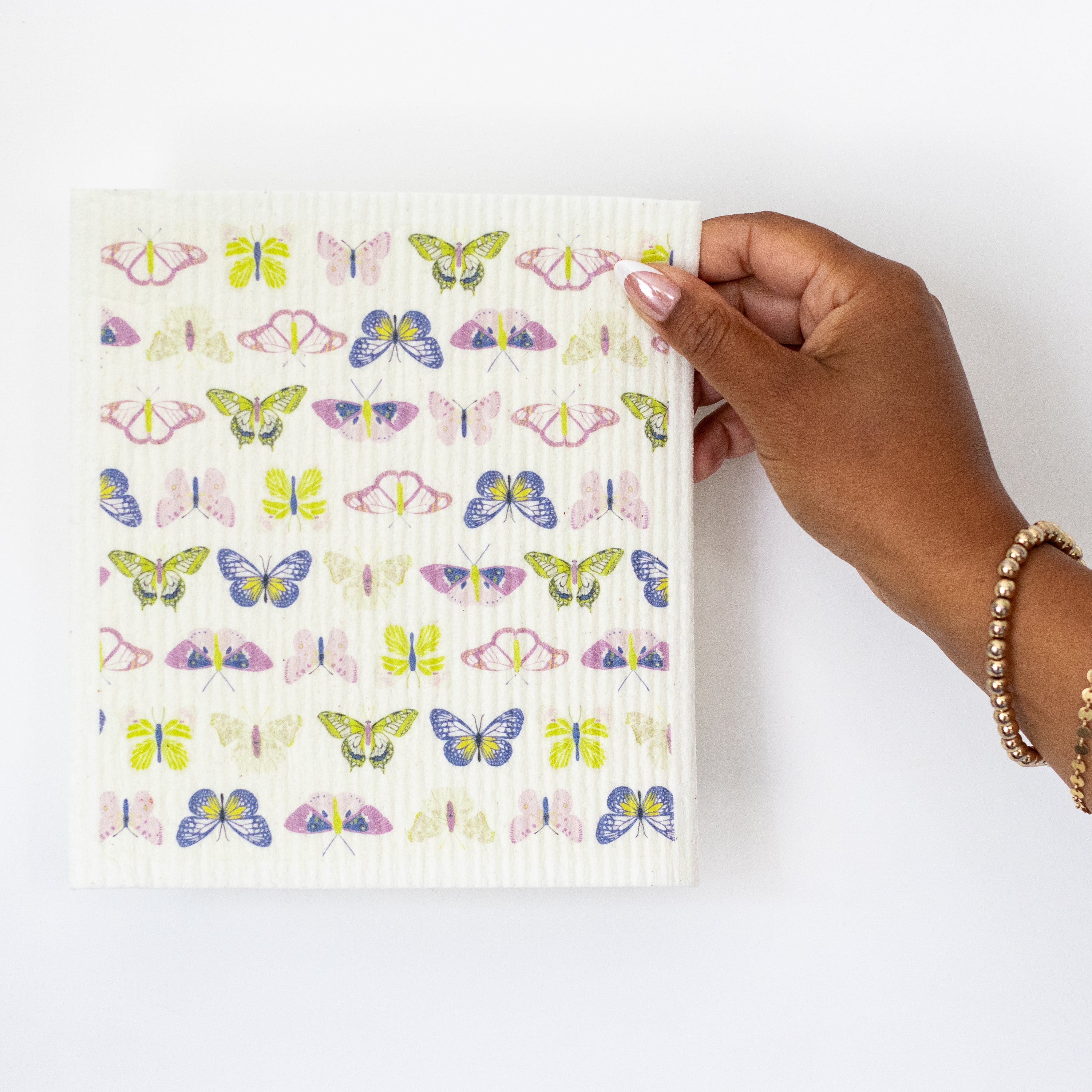 A hand holding a Swedish dishcloth featuring colorful butterfly print in bright green,  blue, and purple.